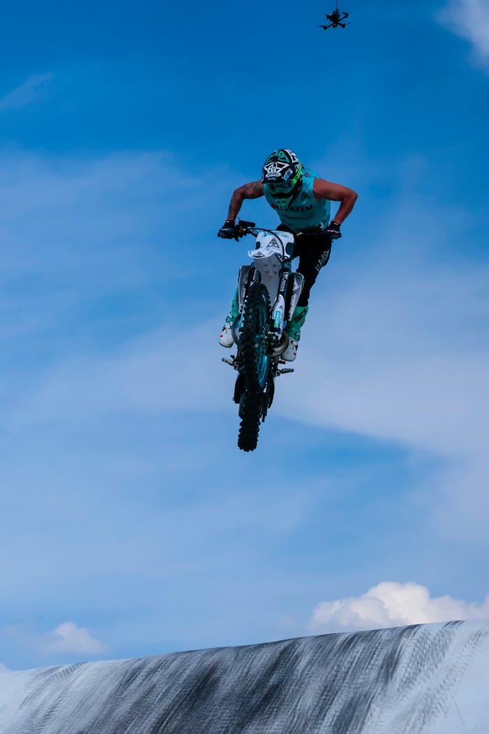 Thrilling motocross stunt in midair, showcasing skill and performance against a blue sky backdrop.