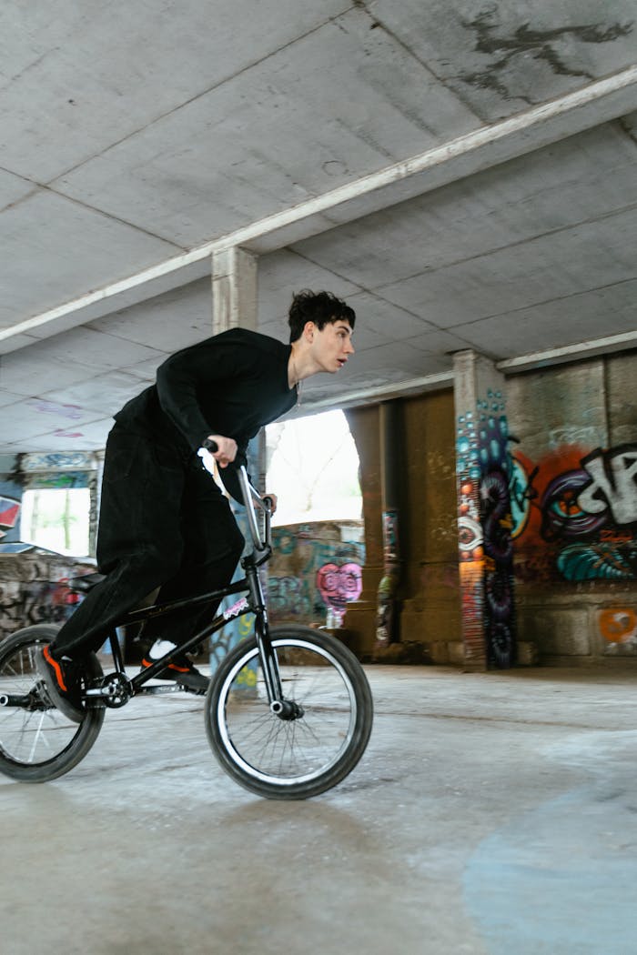 A young man on a BMX bike performing stunts in a graffiti-covered urban skatepark.